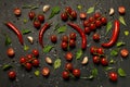 A lot of cherry tomatoes, hot pepper pods, leaves of rucola and salad, garlic and spices lie on a black background