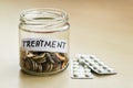 A lot of coins and treatment word in a glass jar near two blisters with pills on a table. Saving money for treatment concept Royalty Free Stock Photo