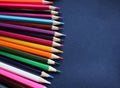 A lot of colored pencils on a dark blue fabric background. Top view, close-up, copy space. Royalty Free Stock Photo