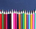 A lot of colored pencils in a row on a dark blue fabric background. Top view, close-up, copy space. Royalty Free Stock Photo