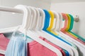 A lot of colorful hangers on a rod, on a white background of the wardrobe.