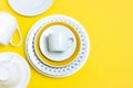 A lot of different ceramic dishes, empty coffee pairs, plates, cups on a bright yellow background