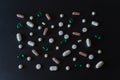 A lot of different pink, green and white coloured pills making mosaic on black matte background. Healthcare and medical concept.