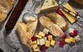 A lot of different types of cheese with dry sausage and fresh bagette, wine glasses on kraft paper.