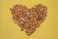 A lot of dried nuts are laid out on a yellow background of textured paper in the shape of a heart. Peeled walnuts, pistachios and