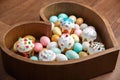 A lot of easter eggs and cake in wooden box heart form on wooden background. Spring and Easter holiday. Minimalistic Royalty Free Stock Photo