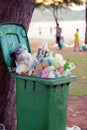 A lot of garbages contained in green wastebin that`s placed under a tree. Public trash background, Garbage waste in park full of a Royalty Free Stock Photo