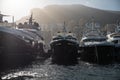 A lot of huge yachts in port of Monaco at sunset, mountain is on background, glossy board of the motor boat, megayachts