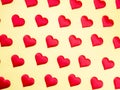 A lot of identical red silk hearts lying staggered on a yellow background. Symbol of love, tenderness and passion Royalty Free Stock Photo