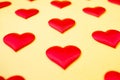 A lot of identical red silk hearts lying staggered on a yellow background. Symbol of love, tenderness and passion Royalty Free Stock Photo