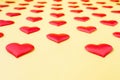 A lot of identical red silk hearts lying staggered on a yellow background. Symbol of love, tenderness and passion Royalty Free Stock Photo