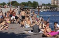 A lot of people sunbathing and bathing in water by the sea in public area of a urban harbor
