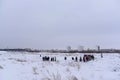 A lot of people take turns walking in the snow on an off-road highway in winter with cameras and selfie sticks