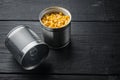 Lot of pieces of canned yellow corn in metall can, on black wooden table background with copy space for text