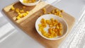 Lot of pieces of canned yellow corn on plate which is on wooden bamboo cutting board on white background. The concept of