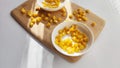 Lot of pieces of canned yellow corn on plate which is on wooden bamboo cutting board on white background. The concept of