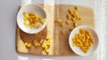 Lot of pieces of canned yellow corn on plate which is on wooden bamboo cutting board on white background. The concept of