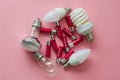 A lot of pink colored batteries and different type of light bulbs are ready for recycling on a pink background