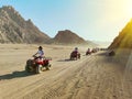 A lot of quad bikes in the dust ride on the background of the wild desert. Sunset in the desert beyond the mountains. ATV rally. Royalty Free Stock Photo
