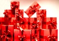 A lot of red gift boxes tied with ribbons on a white wall background. A bunch of gifts in bright festive packaging