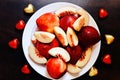A lot of red juicy peaches are cut into pieces, heart-shaped sweets lie on a plate on a wooden table, close-up photo Royalty Free Stock Photo