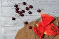 A lot of ripe red cherries on twigs and water melon, lie in a glass plate on a dark blue wooden table Royalty Free Stock Photo