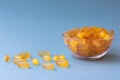 A lot of soft jelly capsules with fish oil as a source of Omega 3 in a transparent bowl on blue background