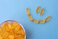 A lot of soft jelly capsules with fish oil as a source of Omega 3 in a transparent bowl on blue background. Smile made of pills f