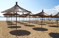 a lot of straw beach umbrellas on the beach, casting a shadow