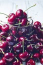 A lot of sweet cherry and a transparent glass on a white table.