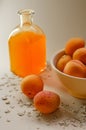 Lots of apricots on a white plate and glass of apricot juice on a white table strewn with oatmeal.