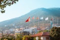 Lots of Europe flags on poles. Mountain in the background and houses nearby. Centered on the Turkey flag. Turkey, Alanya