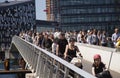 People riding bikes and walking on a modern pedestrian and bicycle bridge in city center by the harbor in sunny weather.