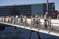 People riding bikes and walking on a modern pedestrian and bicycle bridge in city center by the harbor in sunny weather.