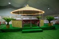 A lounge in the Qatari Bedouin style made of bamboo and next to it two small palm trees and inside it a red majlis with lighting