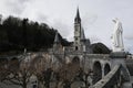 Statue of the Virgin Mary against the background of the Lourdes sanctuary in winter