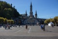 Square with people in front of Sanctuary of Our Lady in Lourdes, France. Famous religious centre of pilgrims.