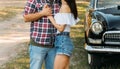 embrace.Love and affection between a young couple at the park, near the old car. a guy in a plaid plane and jeans, a girl in short Royalty Free Stock Photo