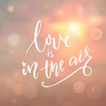 Love is in the air. Romantic quote calligraphy on morning sky with sun and light bokehs.