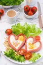 Love breakfast. Fried eggs in heart shaped sausages, lettuce and cherry tomatoes on a plate and a cup of coffee. Vertical view Royalty Free Stock Photo