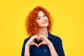 Love. Closeup portrait smiling happy young redhead curly hair woman making heart sign, symbol with hands isolated yellow wall Royalty Free Stock Photo