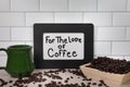 For the Love of coffee sign in black picture frame with green ceramic coffee mug and whole dark roasted coffee beans