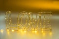Love concept. Valentine`s Day. Wire word LOVE lettering with lighting garland on golden shining holiday background. Copy space