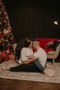 In love couple man and woman sitting on floor cross-legged hugging and kiss Christmas tree Royalty Free Stock Photo