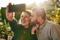 Love, couple and selfie on a patio by happy people kiss, bond and relax at sunset together. Family, phone and man