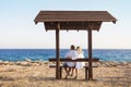 Love couple sitting on a bench by the sea and enjoying beautiful view at sunset Royalty Free Stock Photo