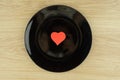 Love dish: scarlet heart in the center of the black plate on light wooden table made of oak
