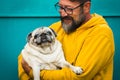 Love dog concept with cheerful adult man hug and hold his own old pug - happy people with animal - colorful yellow and green - Royalty Free Stock Photo