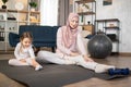 Beautiful muslim mum and cute daughter sitting on the floor mat touching toes on outstretched legs Royalty Free Stock Photo