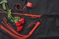 Love games. Top view of bdsm leather kit handcuffs, whip and beautiful red roses against of black silk fabric Royalty Free Stock Photo